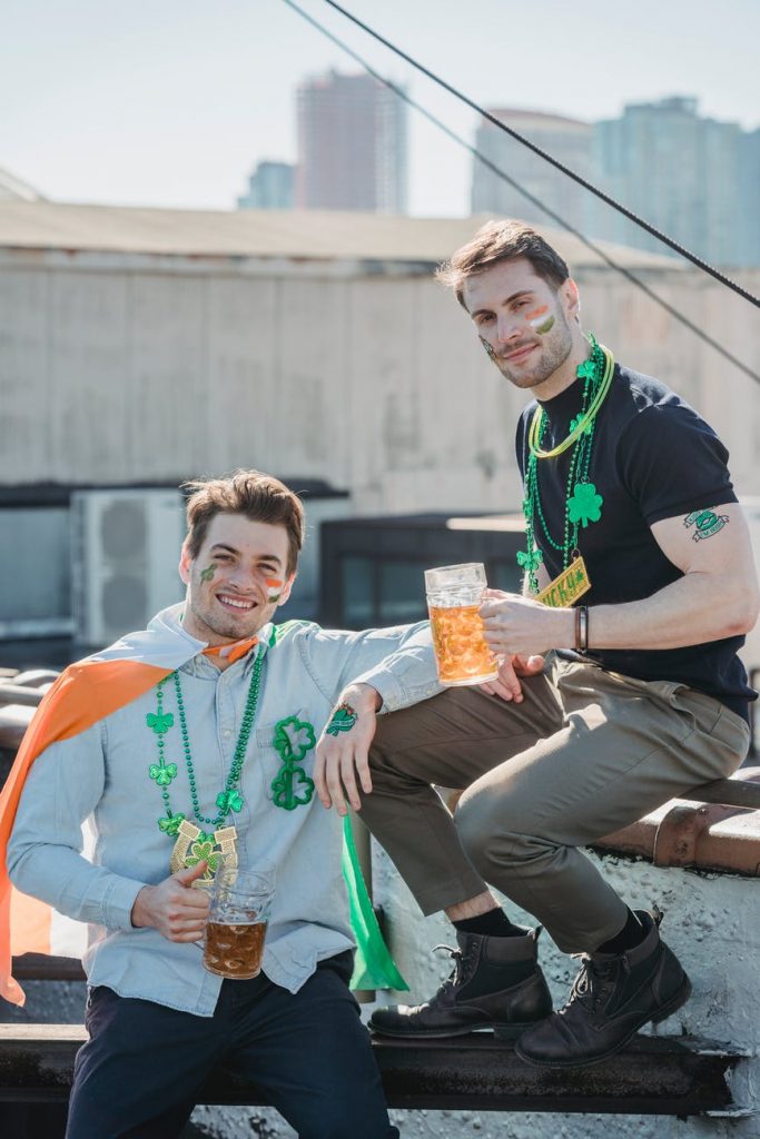 young male friends with mugs of beer celebrating st patricks day on rooftop